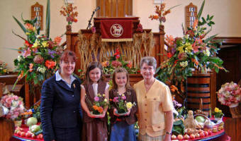 Olivia Black (6) and Sophie Black (5) add their own floral contribution to the beautiful Harvest decorations at Ballinderry Moravian Church last Sunday morning, which included corn arranged in a crisscross display around the front of the pulpit.  Included in the picture are Sr Patsy Holdsworth (left) and Sr Violet Best (right).