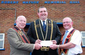 Sir Knt Ian Patterson, Worshipful District Master of Largymore District Chapter RPB No 9 presents a cheque to Sir Knt Stephen Walker of Elijah's Chosen Few Total Abstinence RBP 871. Looking on is Stephen's father, Sir Knt Jack Walker.