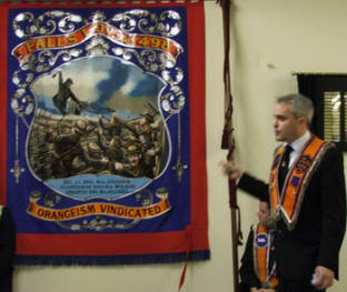 Bro Gary Campbell (Secretary) pictured giving a history of the lodge explaining that the banner, which shows a scene from the Battle of the Somme, also records the names of Sec. Lt. Bro William Graham, Guardsman Bro William Wilson and Trooper Bro William Hillocks, all members of Falls LOL No 498, who laid down their lives in the Great War 1914-1918.
