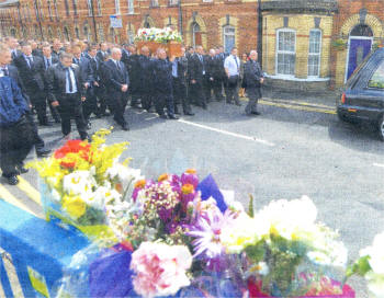 The funeral moves past the floral tributes laid In memoory of Darren Roberts. Photo by Pacemaker