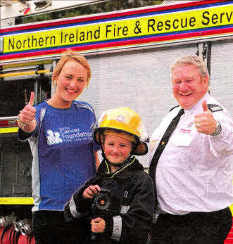 Station Commander Nick Thompson, Northern Ireland Fire and Rescue Service and Jan Caldwell, Cancer Prevention Assistant, Ulster Cancer Foundation pictured with Darren Dumigan, from Harmony Hill Primary School 
