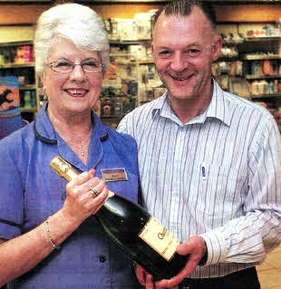 Jean Logan who has retired after 53 years in Crumlin Pharmacy being presented with a bottle of champagne by pharmacist Philip Cartmill. U55211-101AO