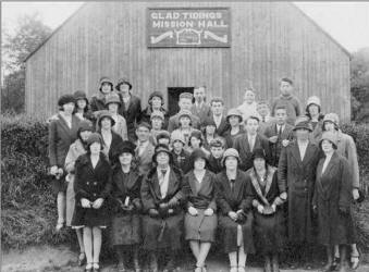 Pictured at The Glad Tidings Mission Hall at the Mills, Dromore in about 1930 are L to R:  (front row) Maisie Jackson, Mrs. Magill, Miss Morrell – Missionary, Miss Hearsey, Mrs. Thomas, Mrs. Hunter, Mrs. Miskimmons and Miss Lilley.  (second row)  Barbara Ireland, Ena Purdy, Sammy Lunn, Minnie Beggs, Madge Miskimmons, Tina Jackson, Willie Purdy, Bobby Baxter, Sam Miskimmons, Evelyn Harvey and Mary Emily Harvey. 
